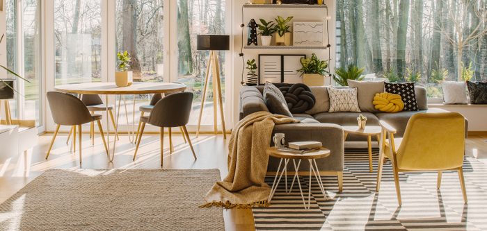 Spacious living room interior with a corner sofa and armchair next to a dining table with chairs standing by the window ©GroundImage