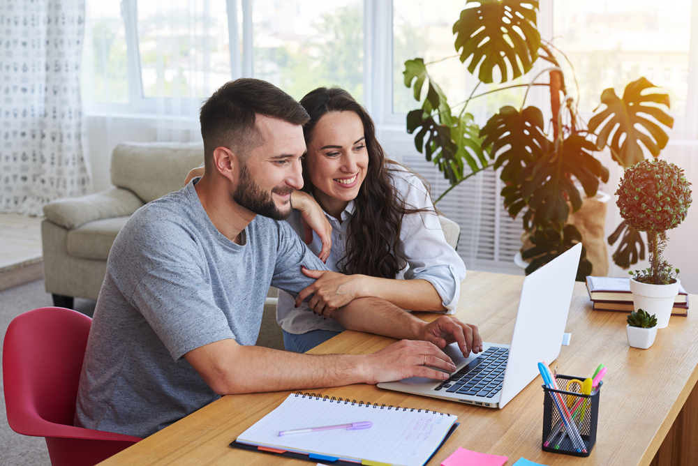 Wide shot of smiling couple surfing on laptop sitting at table ©ArtFamily