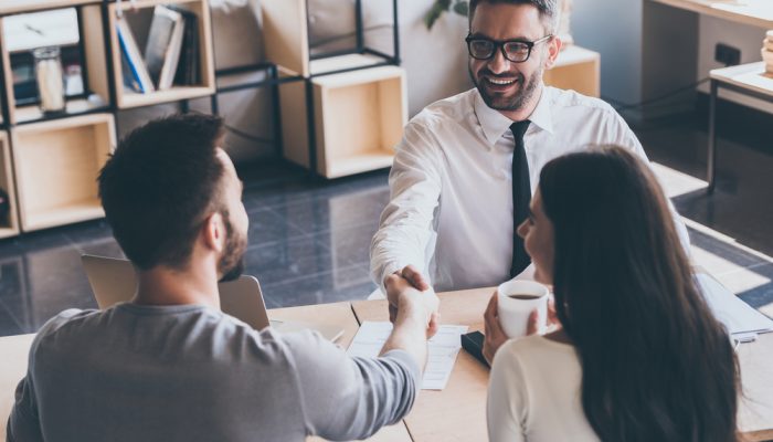 Real estate agents shaking hands with man while young woman looks at them and smiling ©G-Stock Studio